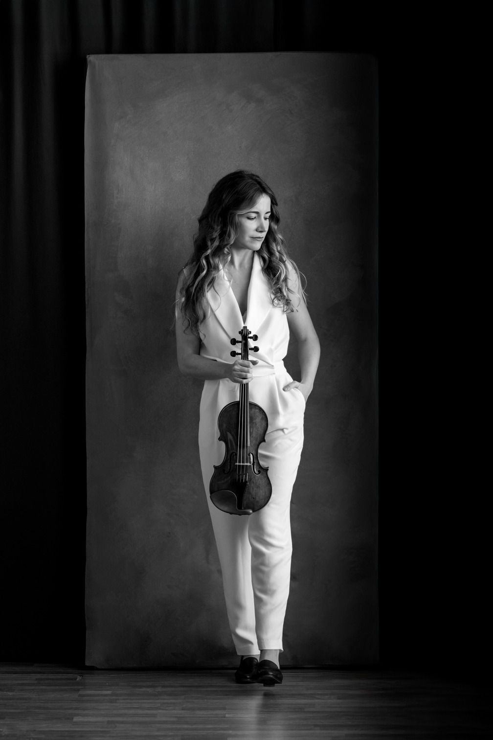 Laura Gallego, de cuerpo entero y en blanco y negro, con el violín en la mano sobre un fondo gris de estudio